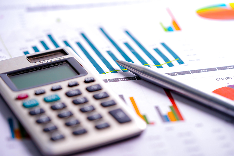 Calculator with pen and shows budget graphs regarding finance and budgets.