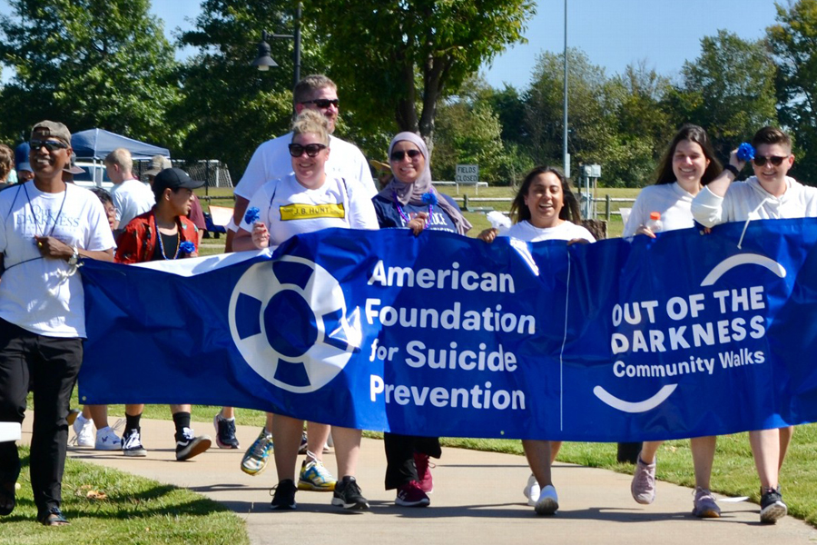 Group of people walking with a banner that says American Foundation for Suicide Prevention, Out of the Darkness Community Walks.